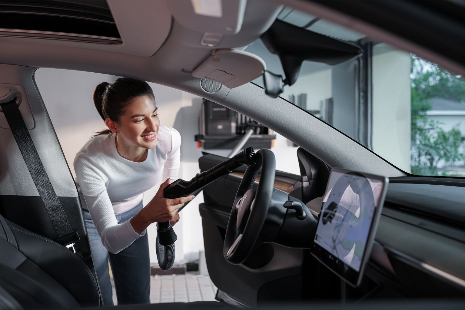 A girl is using the Grandstorm Retractable Vacuum Cleaner to vacuum and wash her car steering wheel.